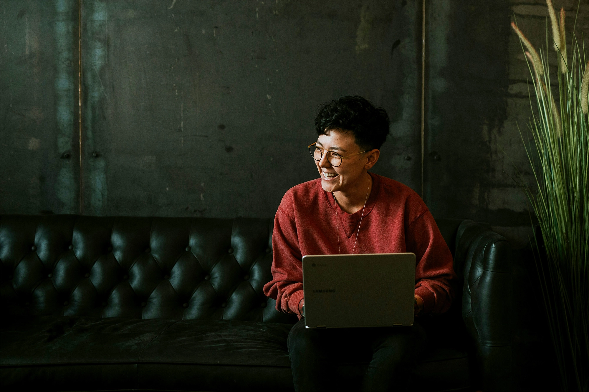 Person smiling siting on a couch with a laptop on their lap